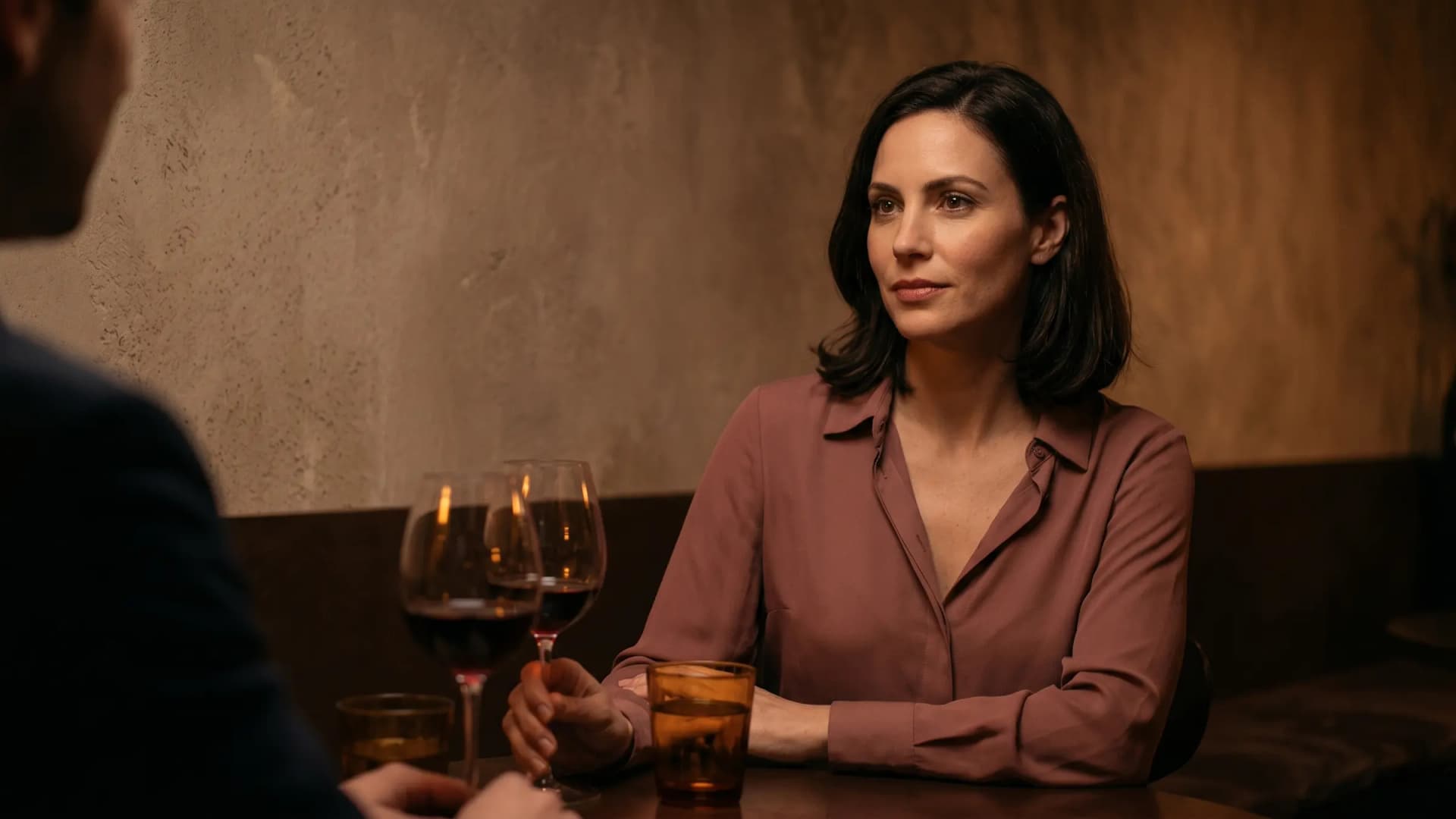A woman sitting in a low-lit wine bar with a calm, observant expression