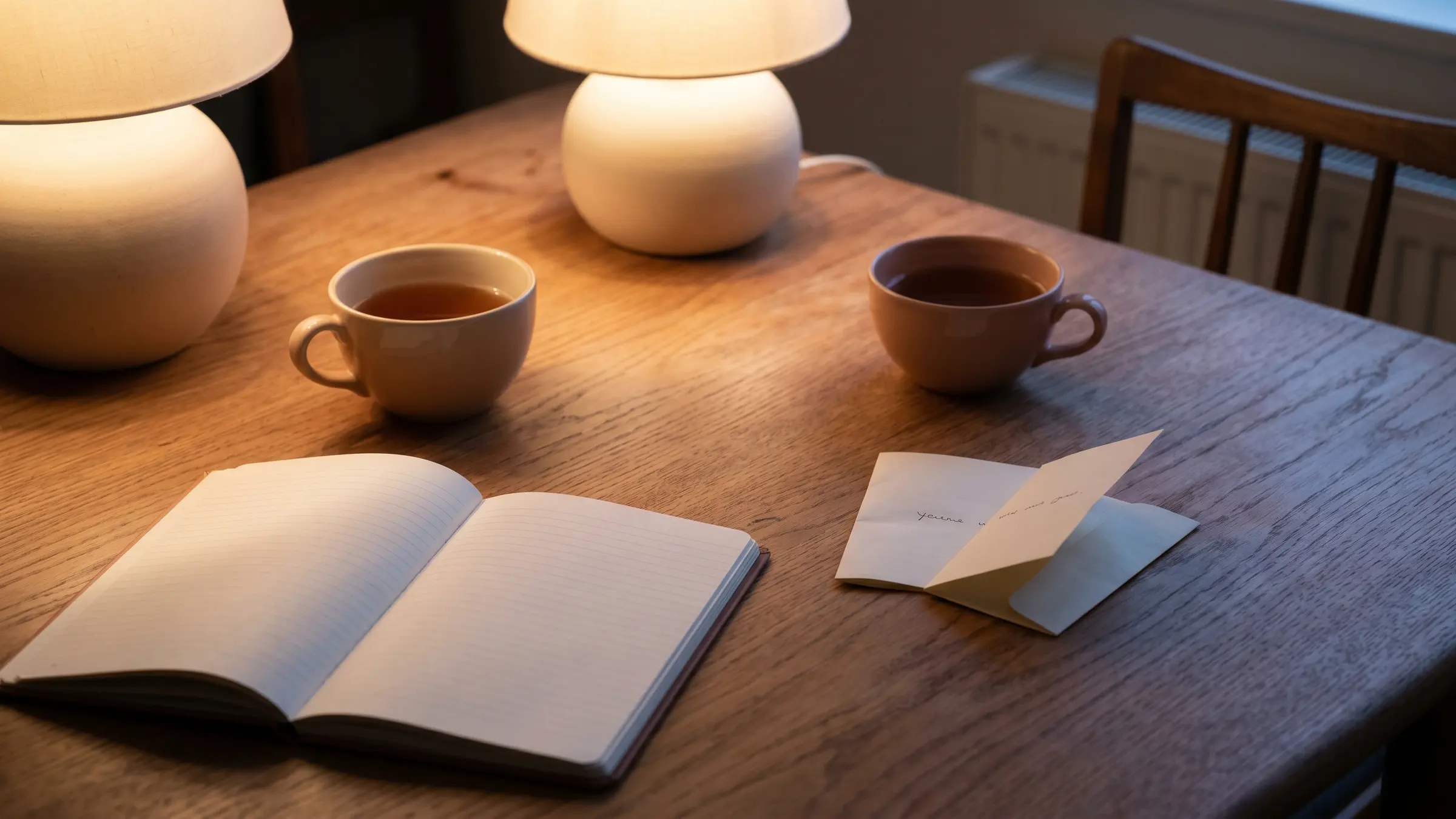 Two cups of tea and an open notebook on a dining table at dusk
