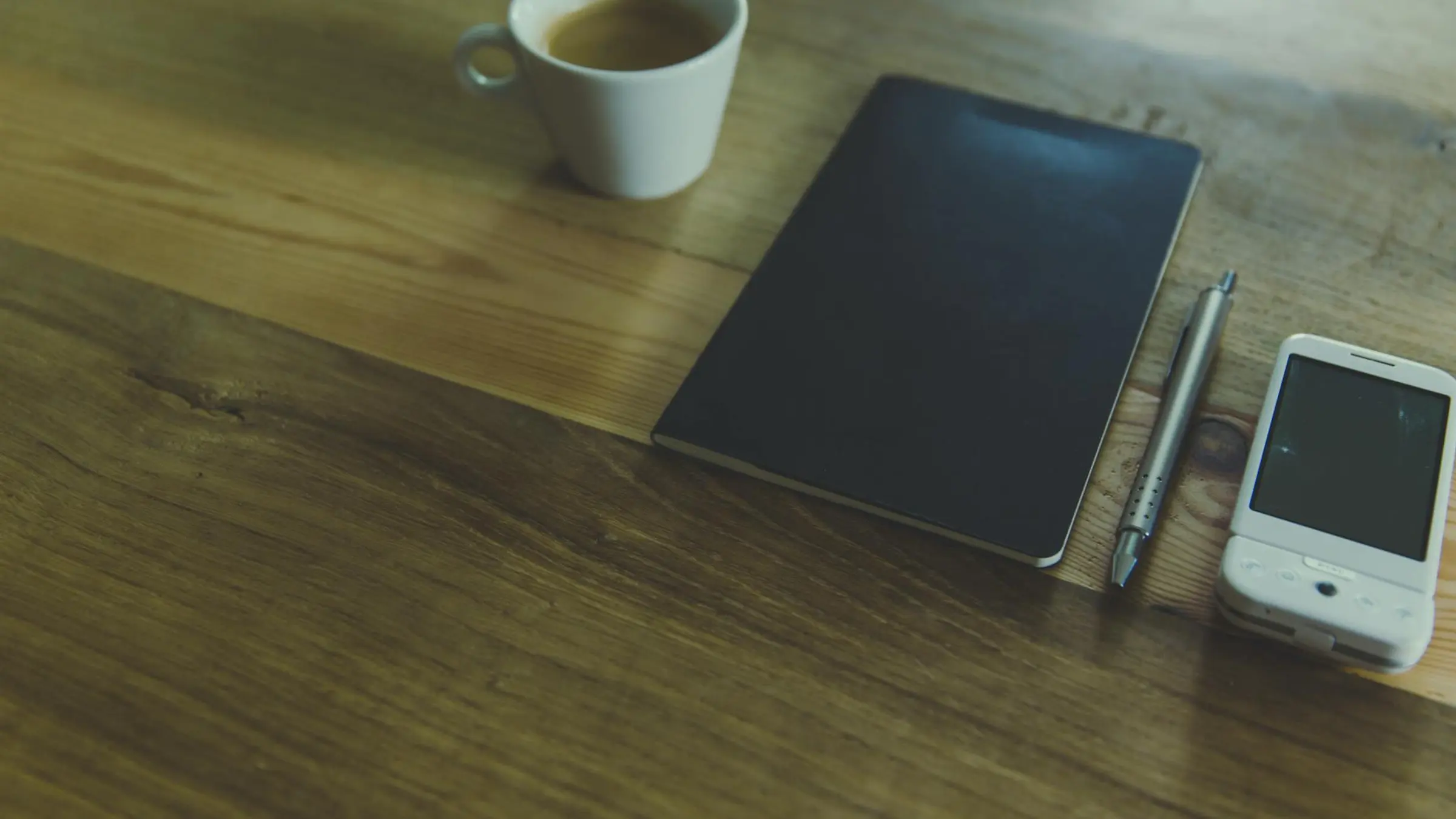 A quiet phone on a table beside a folded note and warm window light, suggesting a careful breakup message