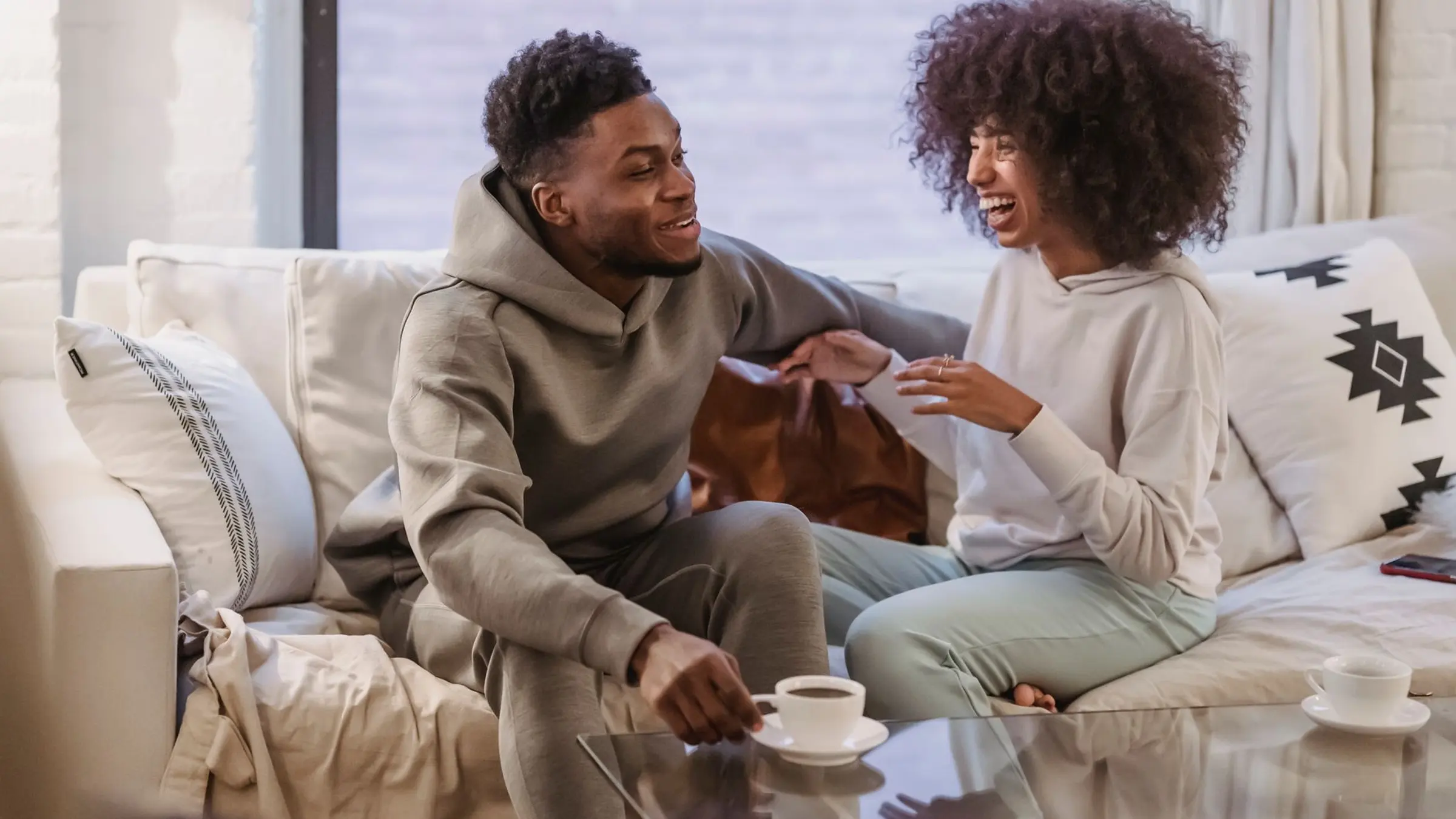 Two people sitting apart on a quiet sofa with tea and a notebook, giving each other calm space during a relationship pace conversation